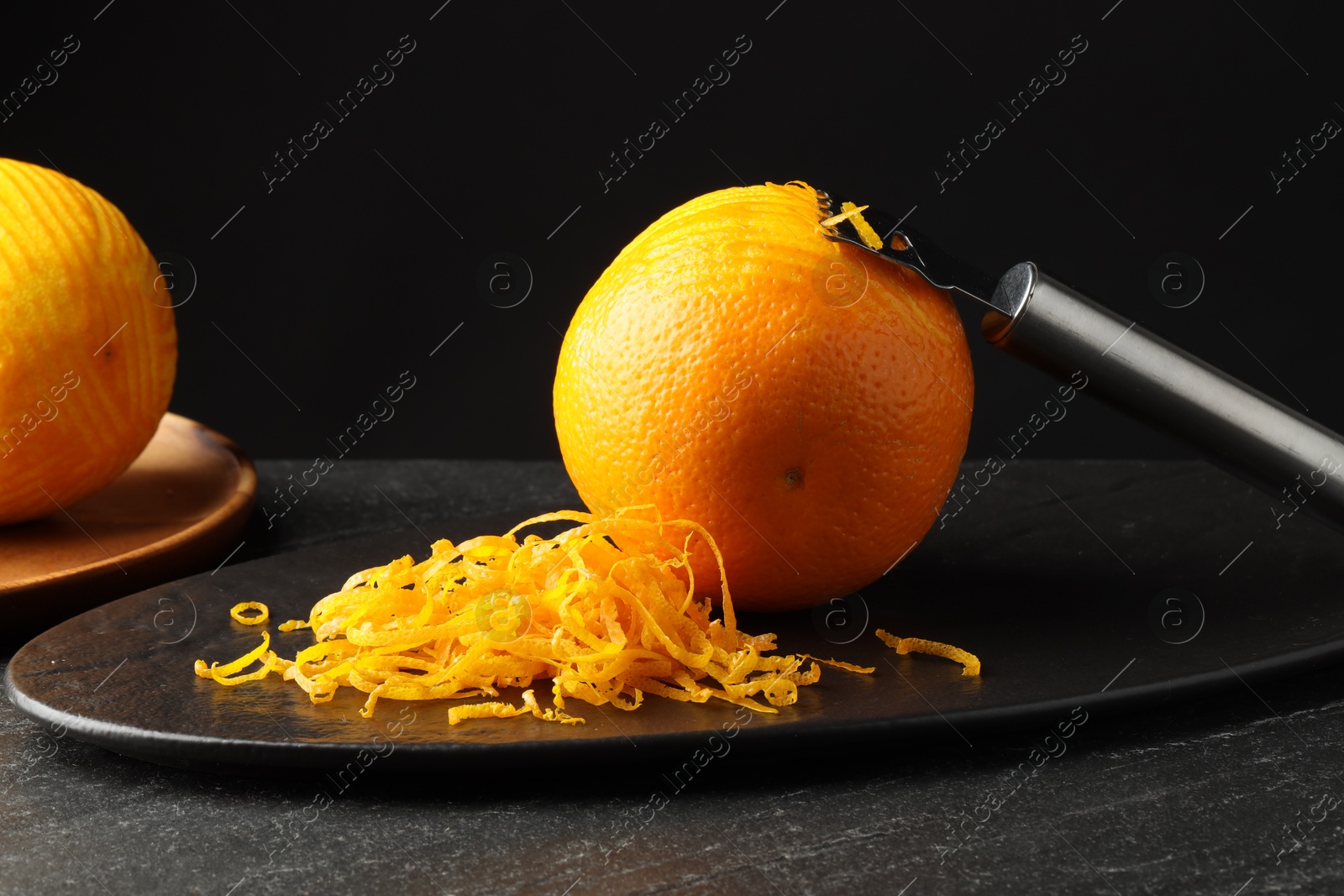 Photo of Fresh orange zest, zester and fruits on black table