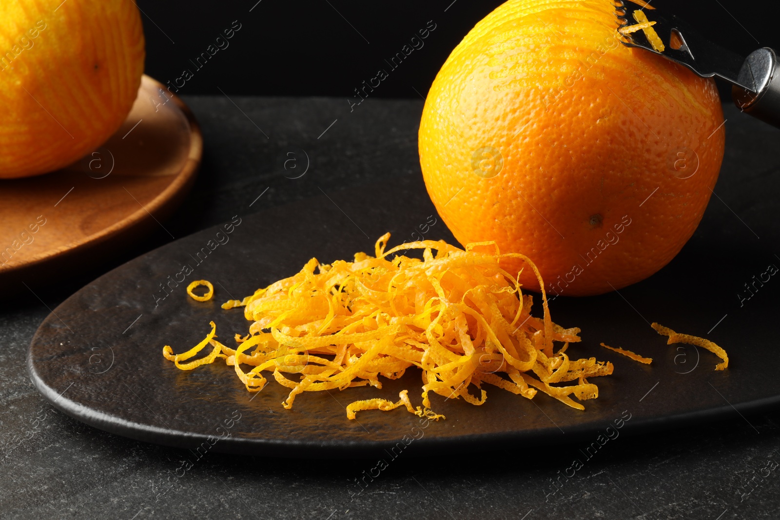 Photo of Fresh orange zest, zester and fruits on black table