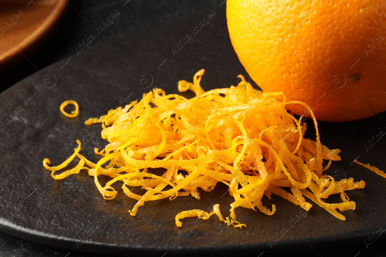 Photo of Fresh orange zest and fruit on black table, closeup