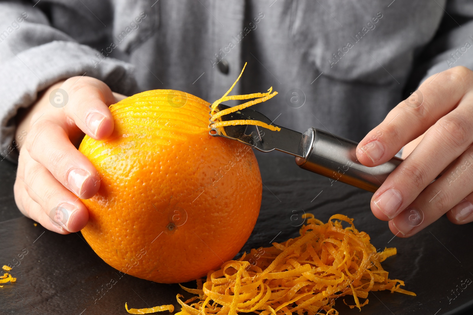 Photo of Woman zesting orange at black table, closeup