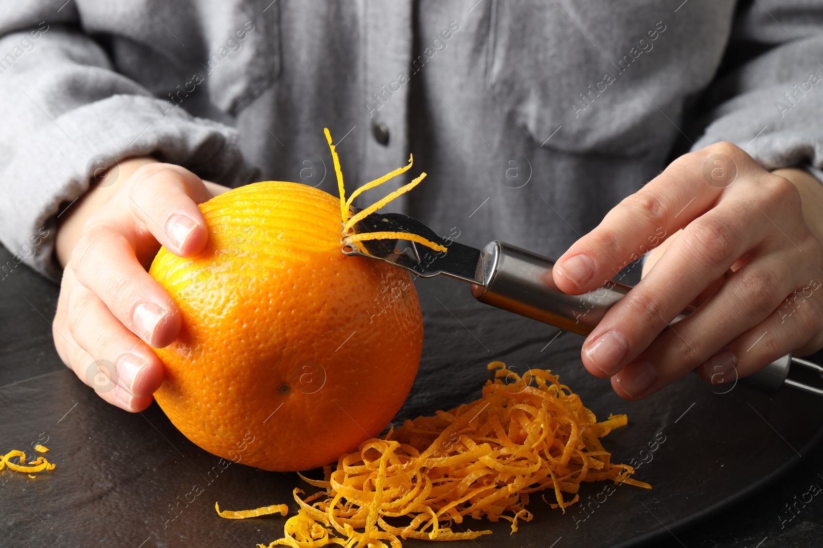 Photo of Woman zesting orange at black table, closeup