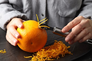 Photo of Woman zesting orange at black table, closeup