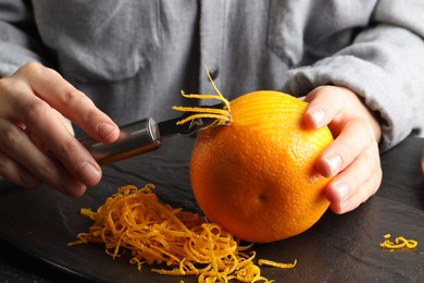 Photo of Woman zesting orange at black table, closeup