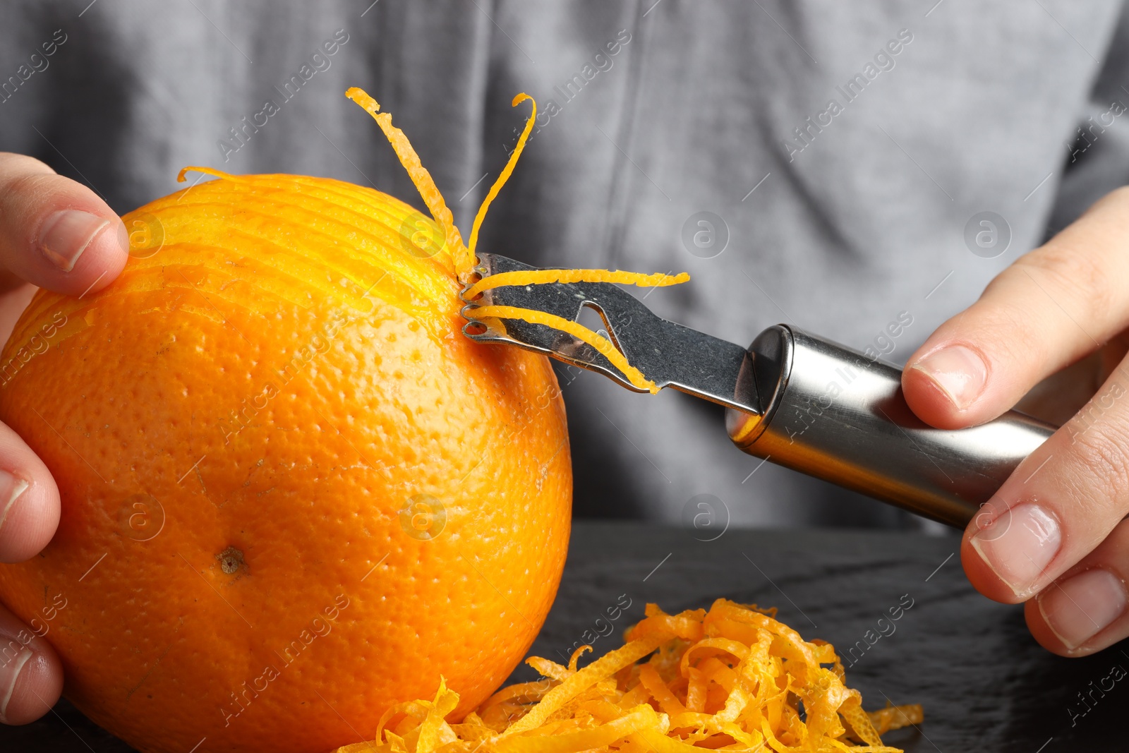 Photo of Woman zesting orange at black table, closeup