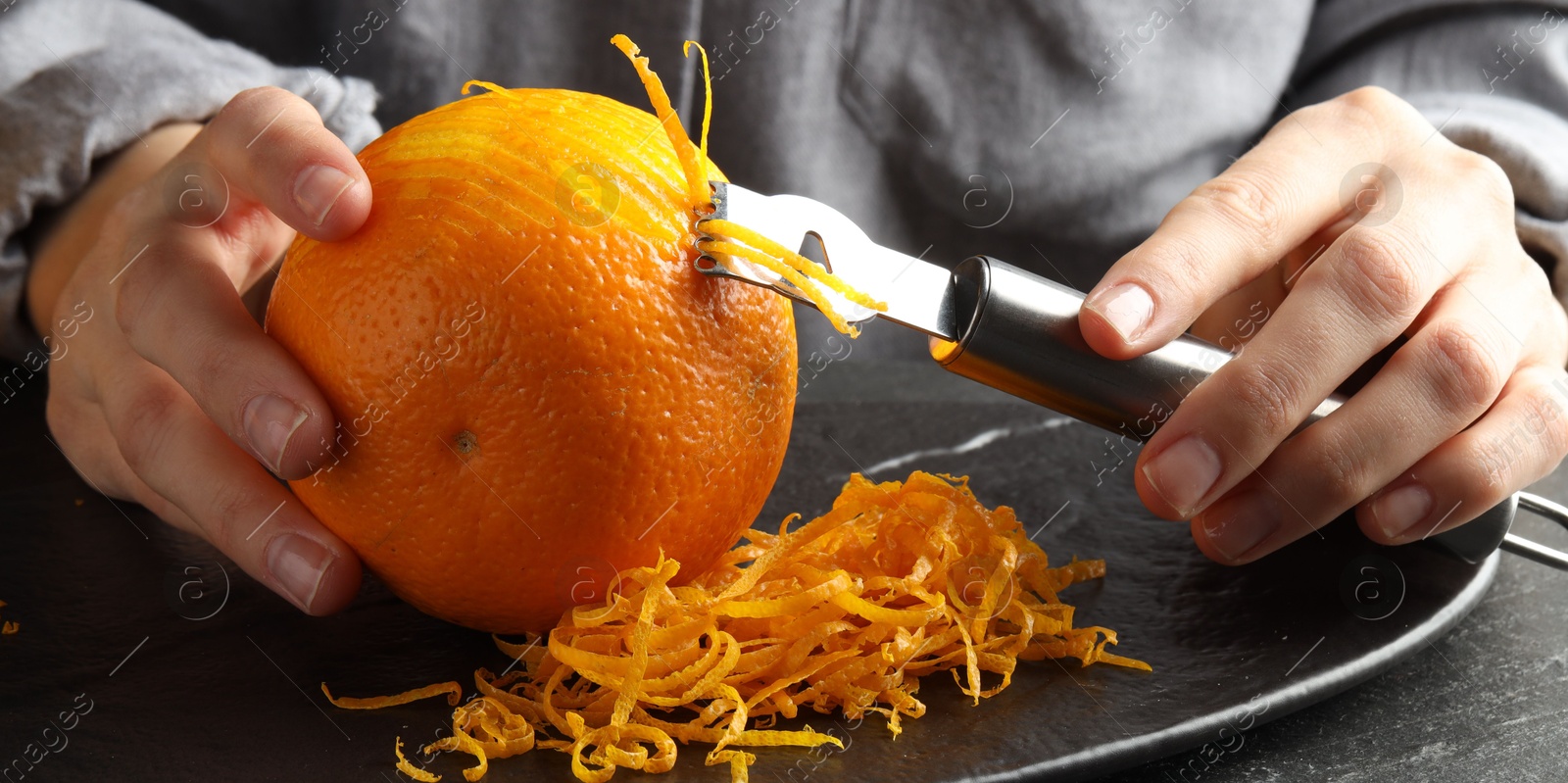 Photo of Woman zesting orange at black table, closeup