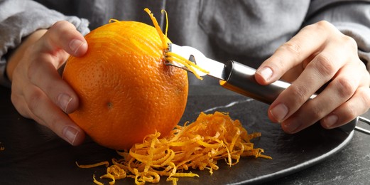 Photo of Woman zesting orange at black table, closeup