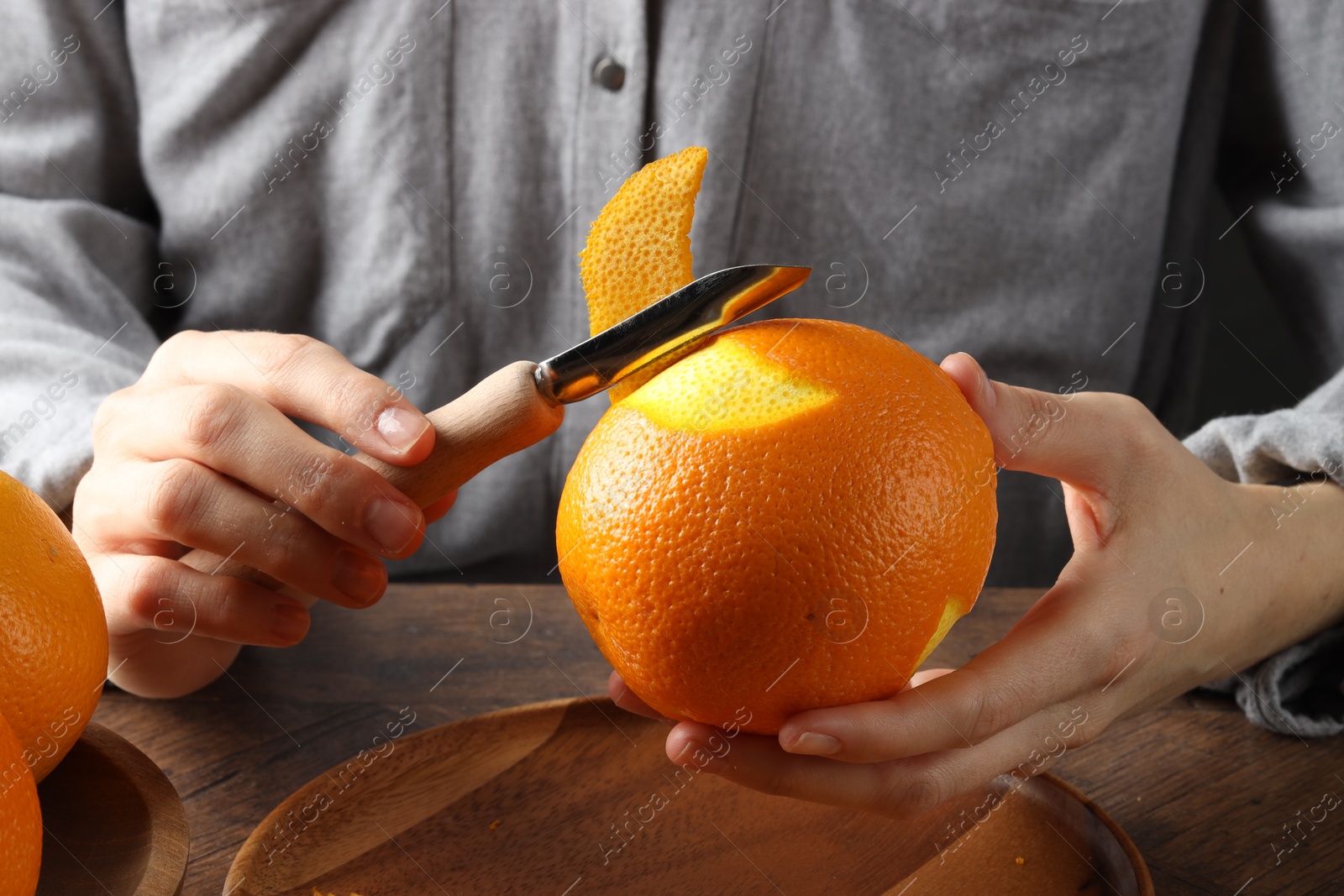 Photo of Woman zesting orange at wooden table, closeup