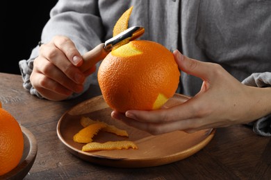 Photo of Woman zesting orange at wooden table, closeup