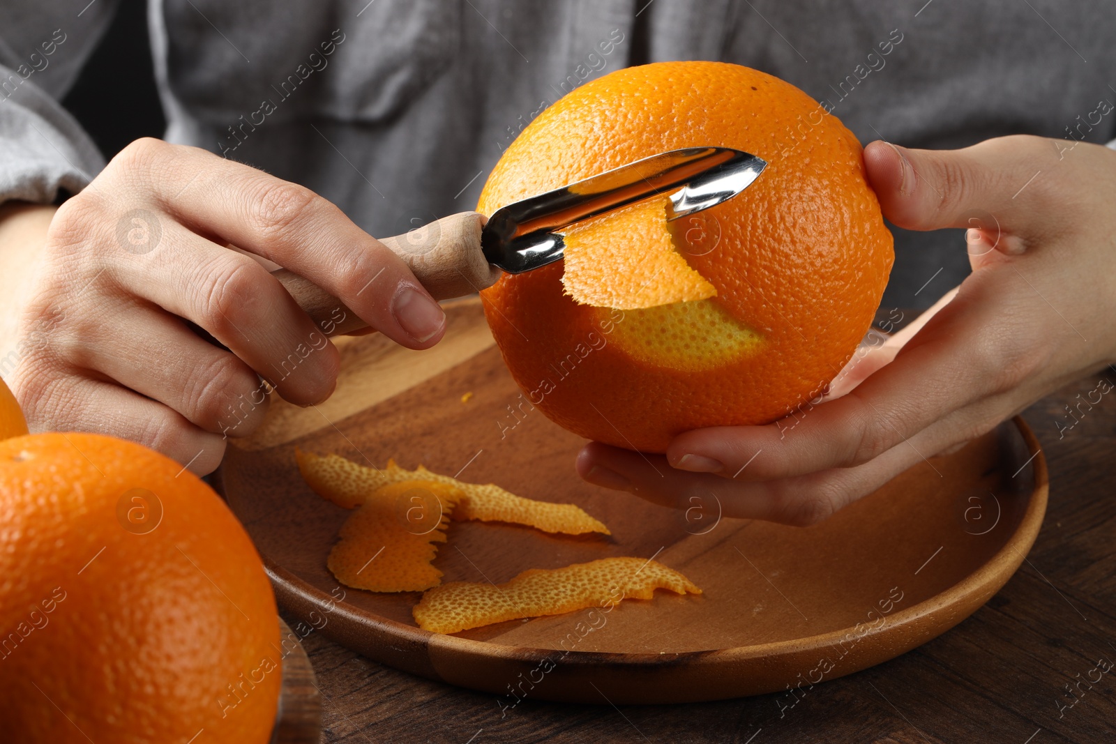 Photo of Woman zesting orange at wooden table, closeup