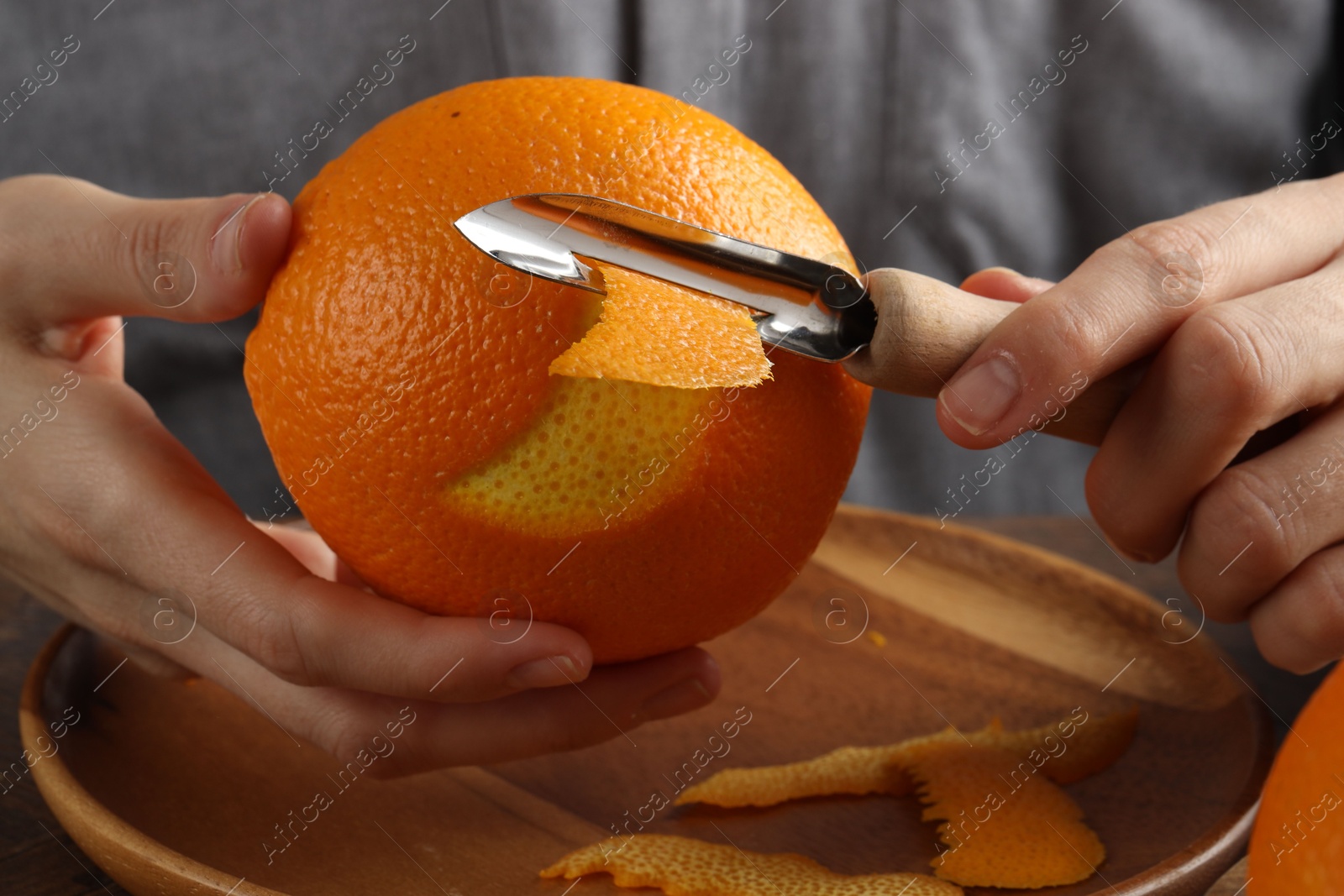 Photo of Woman zesting orange at wooden table, closeup