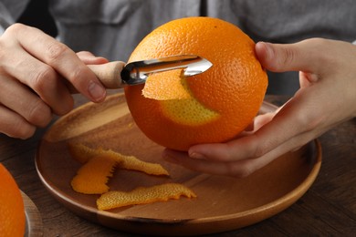 Photo of Woman zesting orange at wooden table, closeup