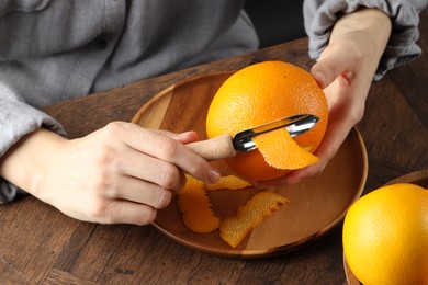 Woman zesting orange at wooden table, closeup