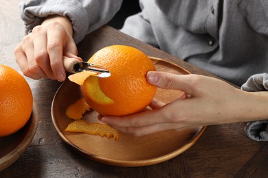 Photo of Woman zesting orange at wooden table, closeup