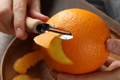 Photo of Woman zesting orange at wooden table, closeup