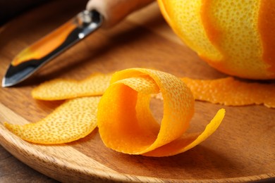 Photo of Fresh orange peel, channel knife and fruit on wooden table, closeup