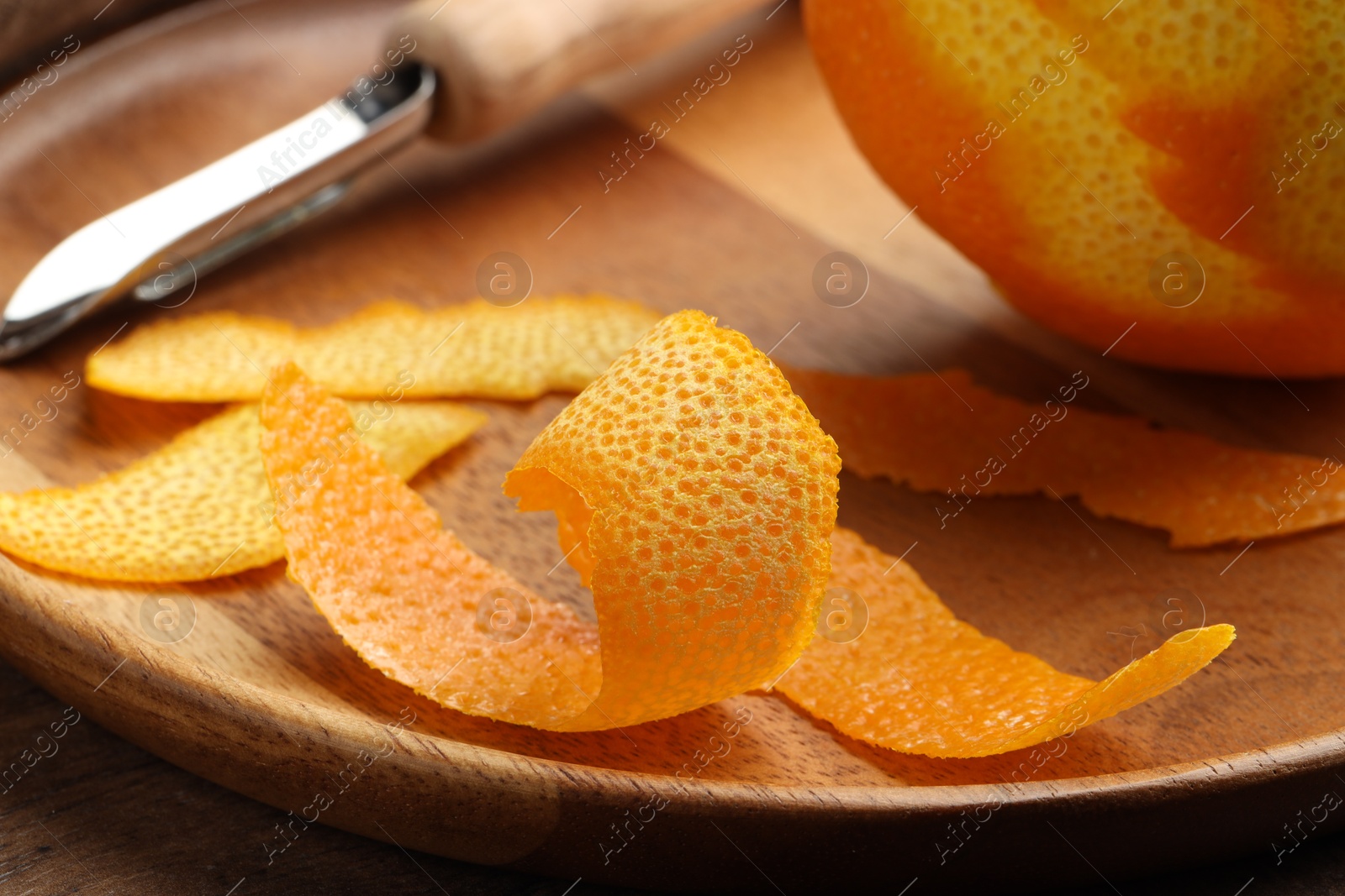 Photo of Fresh orange peel, channel knife and fruit on wooden table, closeup