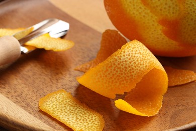 Photo of Fresh orange peel, channel knife and fruit on wooden table, closeup