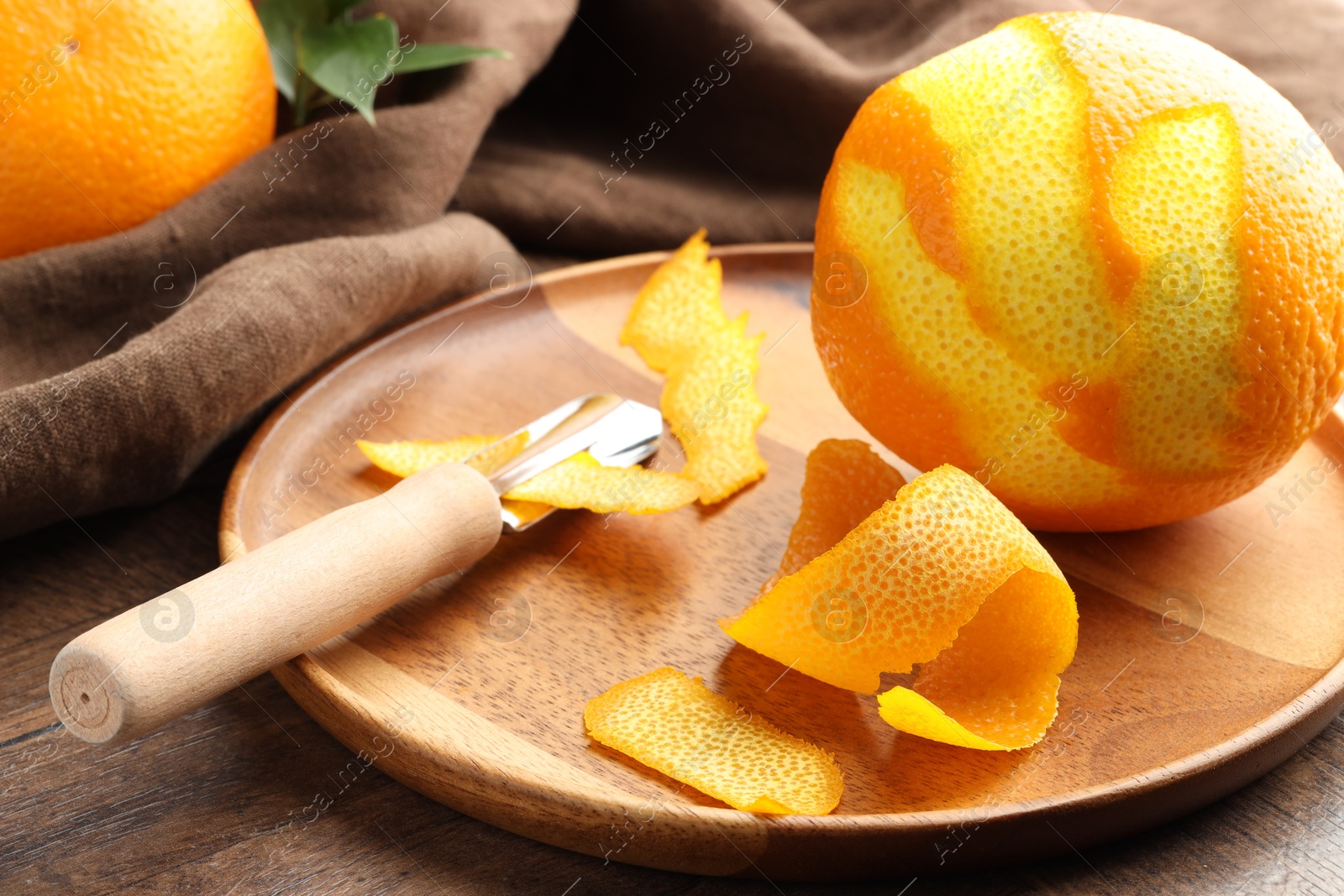 Photo of Fresh orange peel, channel knife and fruit on wooden table, closeup