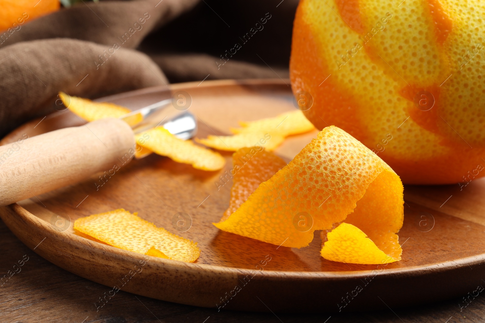 Photo of Fresh orange peel, channel knife and fruit on wooden table, closeup