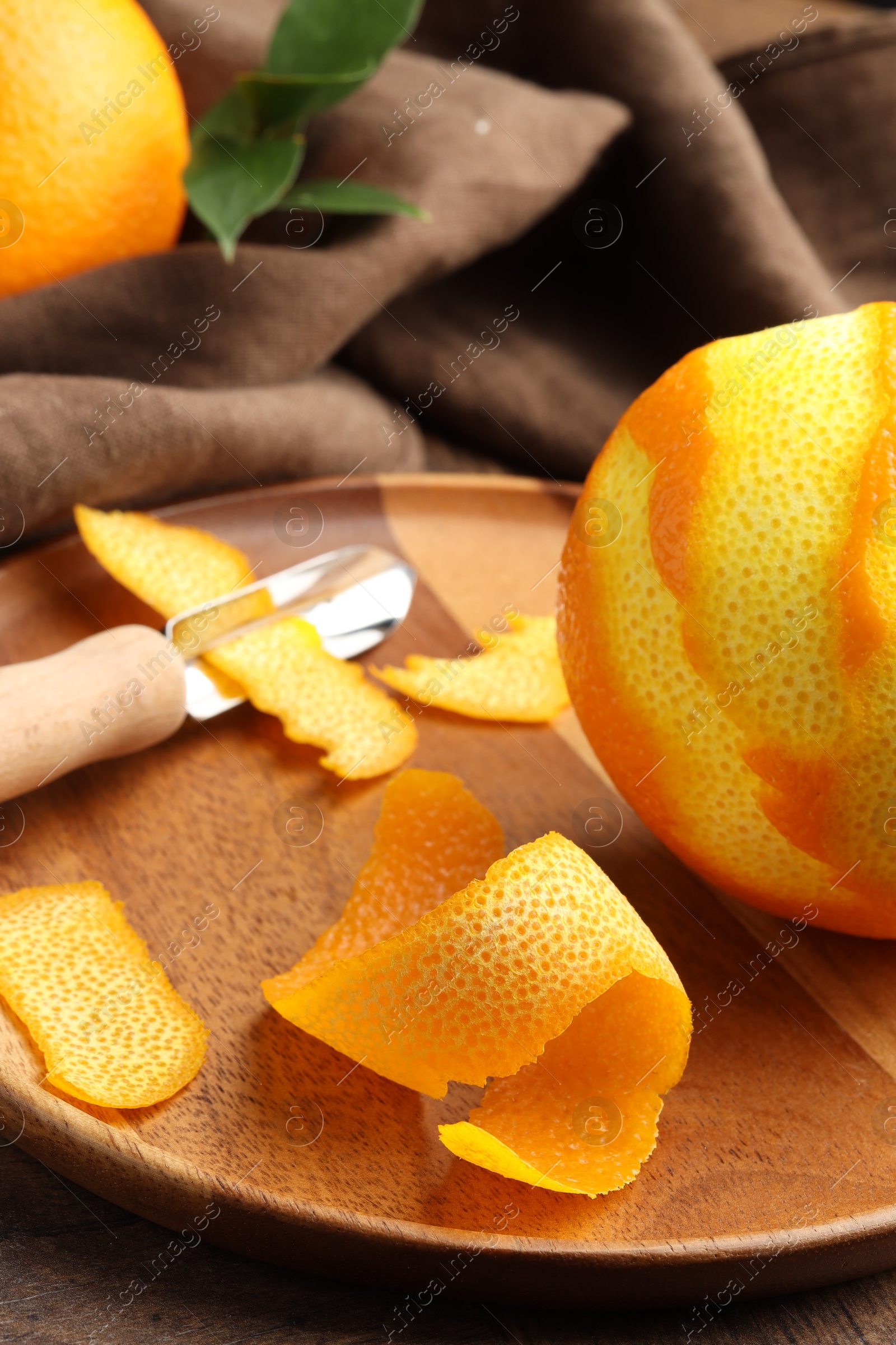 Photo of Fresh orange peel, channel knife and fruit on wooden table, closeup