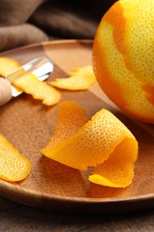 Photo of Fresh orange peel, channel knife and fruit on wooden table, closeup