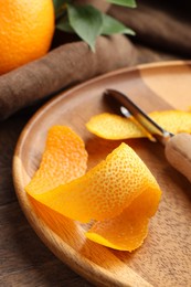 Photo of Fresh orange peel and channel knife on wooden table, closeup