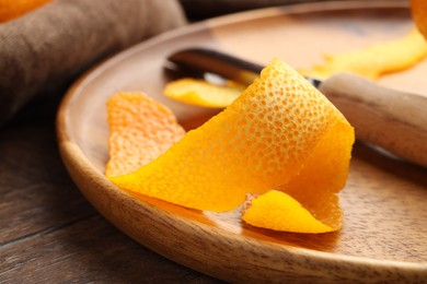 Photo of Fresh orange peel and channel knife on wooden table, closeup