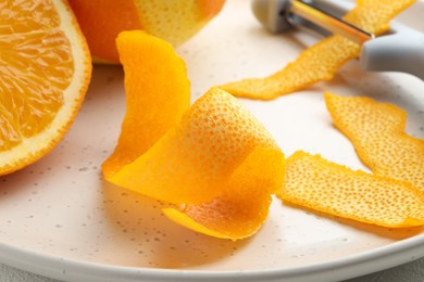 Photo of Fresh orange peel, fruit and peeler on table, closeup