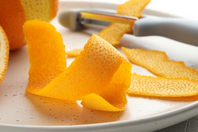 Fresh orange peel and peeler on table, closeup