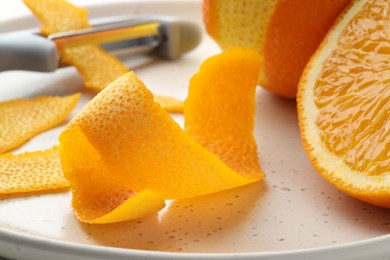 Photo of Fresh orange peel, fruit and peeler on table, closeup