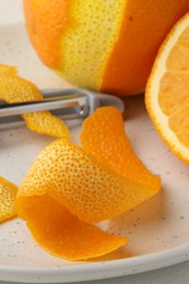 Photo of Fresh orange peel, fruit and peeler on light table, closeup