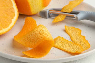 Photo of Fresh orange peel, fruit and peeler on light table, closeup