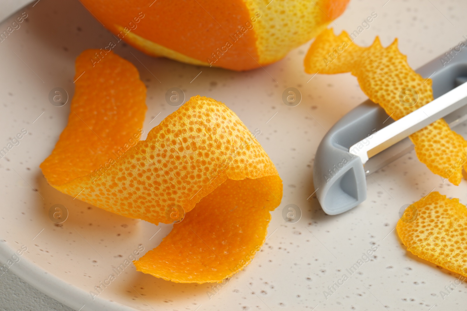 Photo of Fresh orange peel, fruit and peeler on light table, closeup