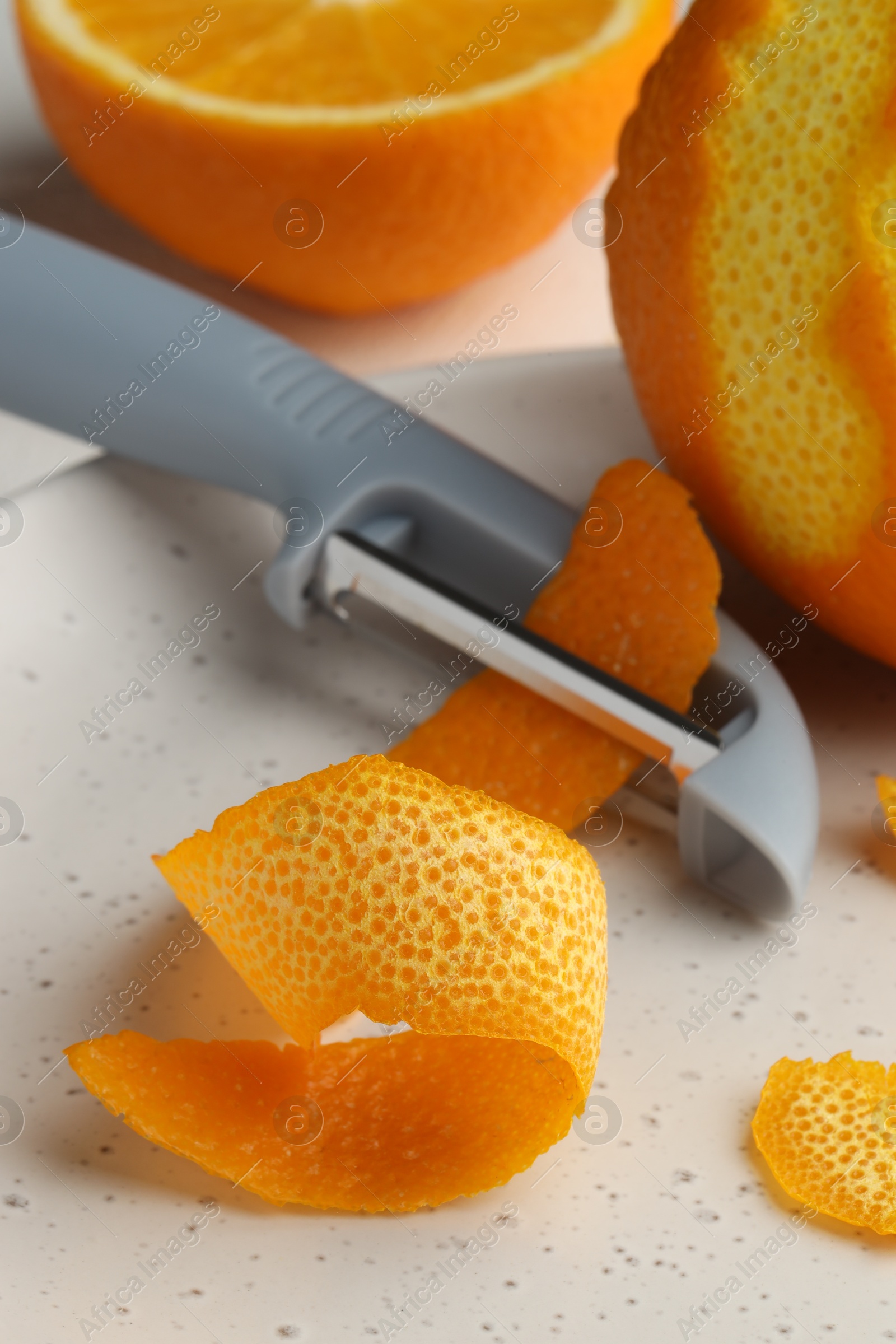 Photo of Fresh orange peel, fruit and peeler on table, closeup