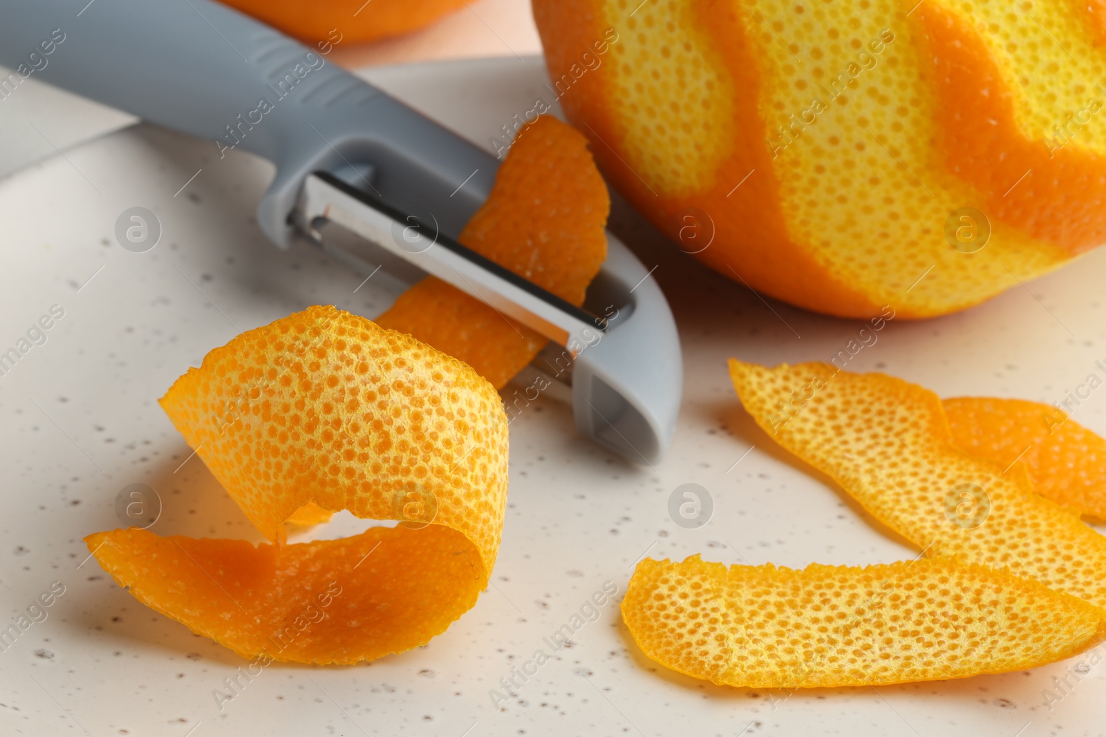 Photo of Fresh orange peel, fruit and peeler on table, closeup