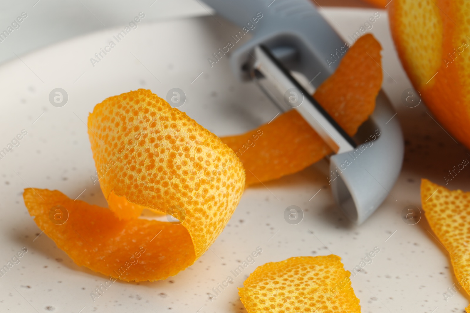 Photo of Fresh orange peel, fruit and peeler on table, closeup