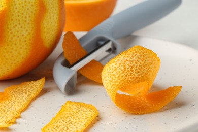 Photo of Fresh orange peel, fruit and peeler on table, closeup