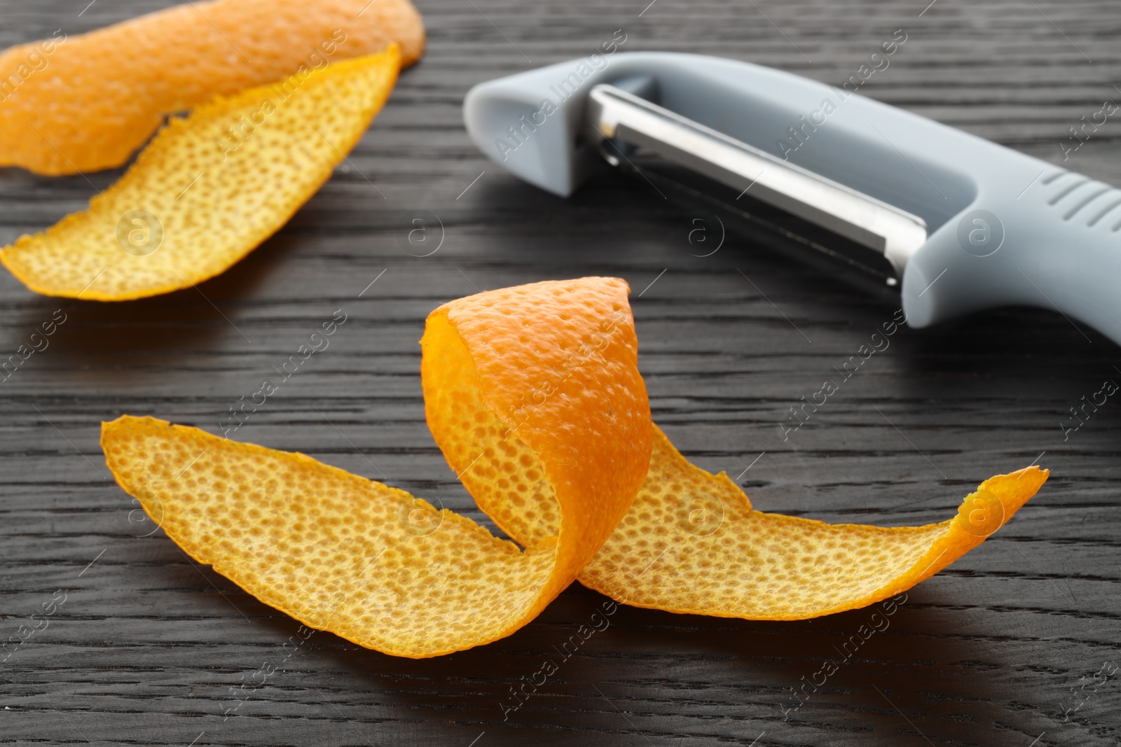 Photo of Fresh orange peels and peeler on wooden table, closeup