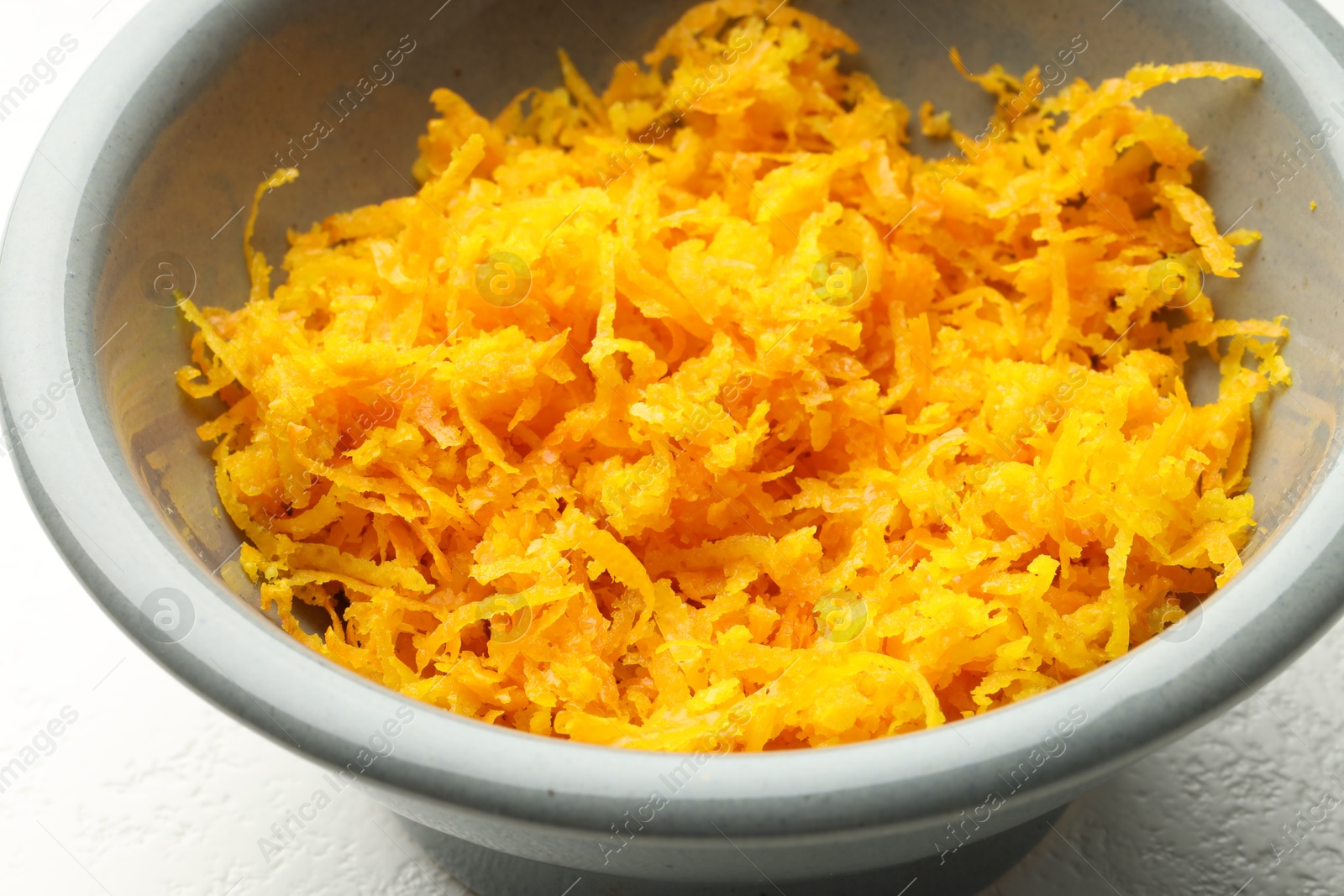 Photo of Fresh orange zest in bowl on light table, closeup