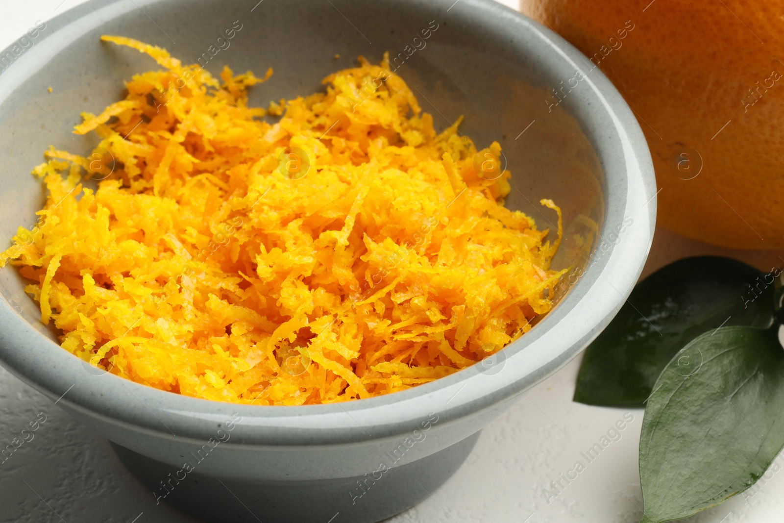 Photo of Fresh orange zest in bowl on light table, closeup