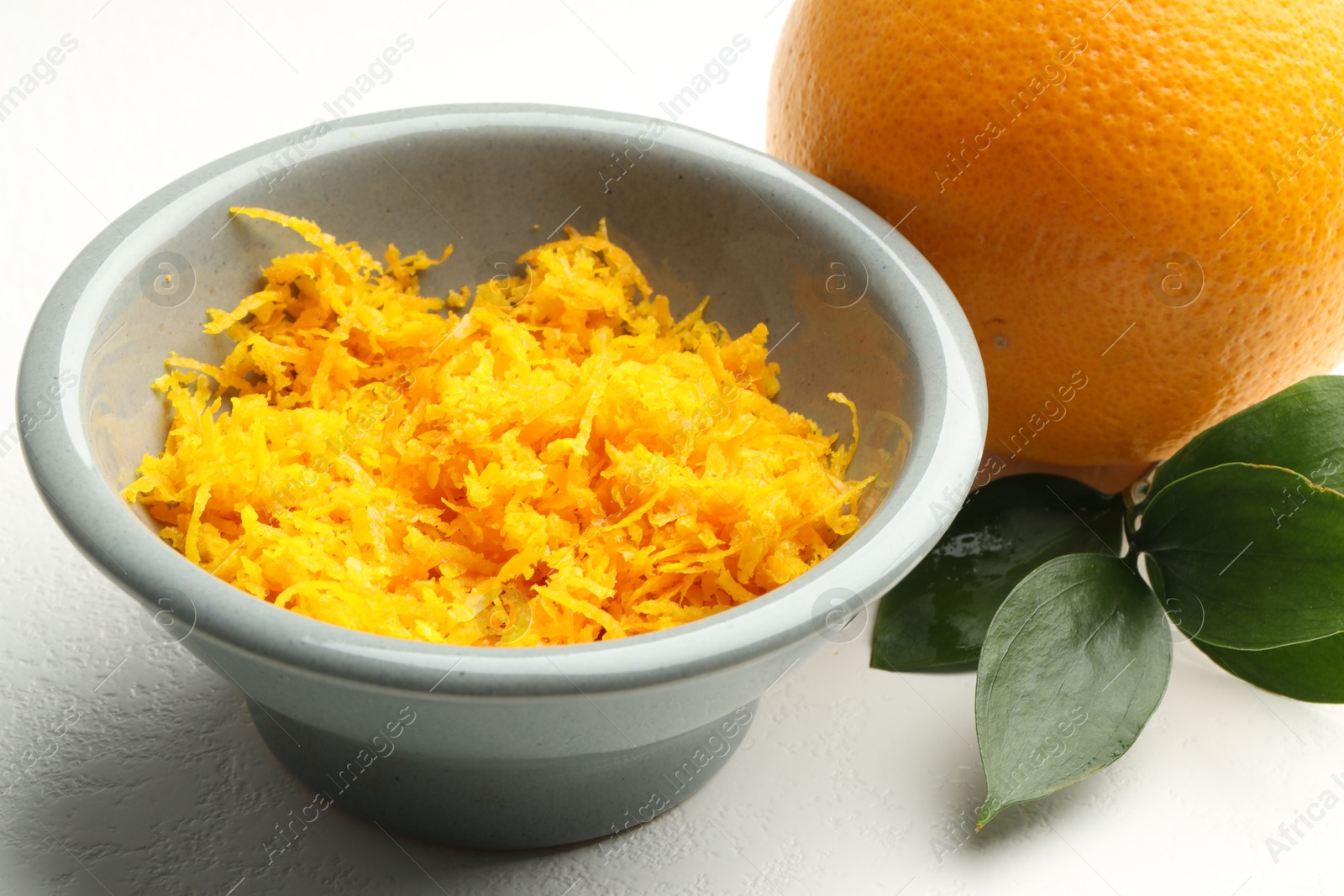 Photo of Fresh orange zest in bowl on light table, closeup