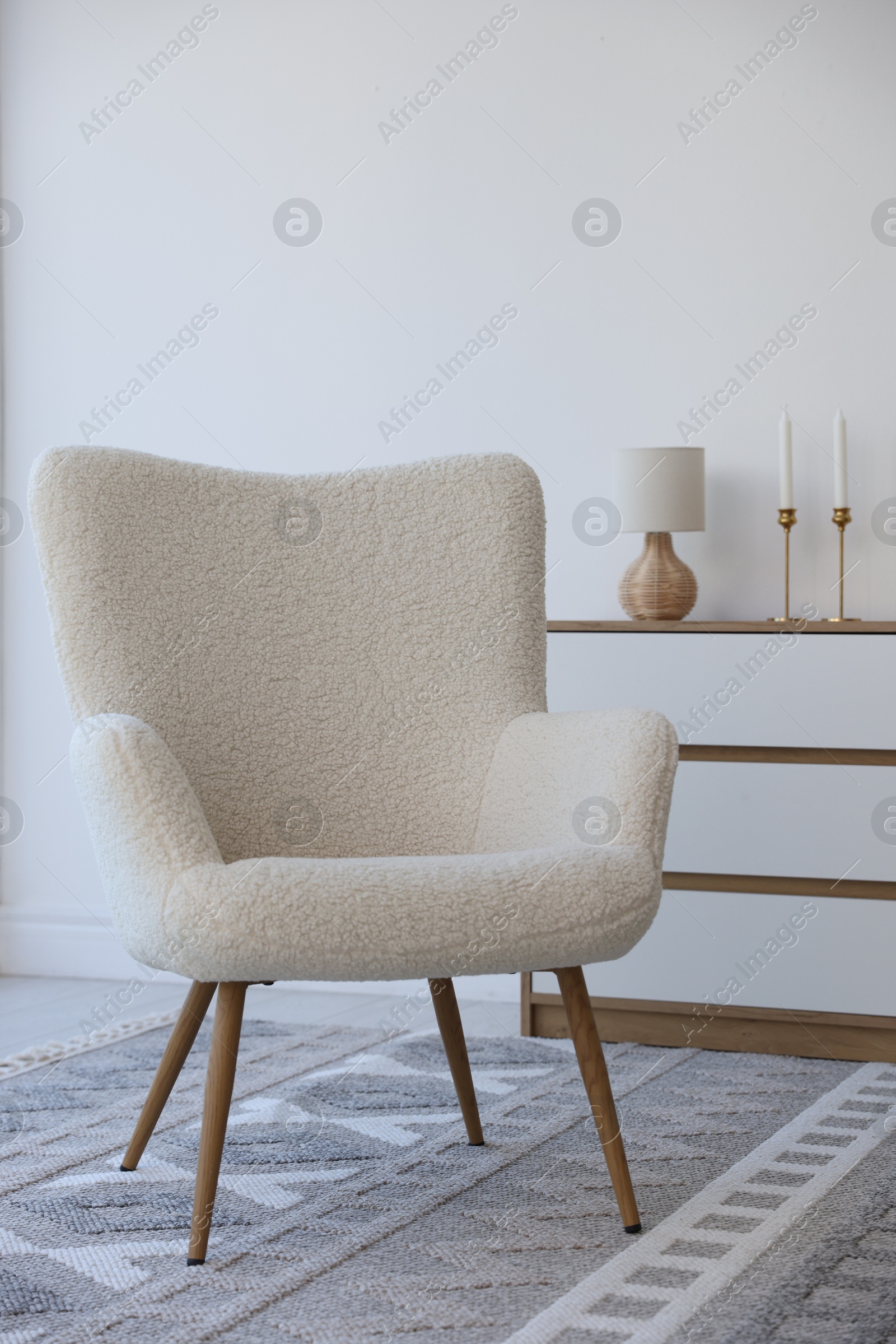 Photo of Soft armchair and chest of drawers near white wall indoors