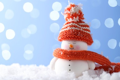 Photo of Cute decorative snowman on artificial snow against light blue background, space for text