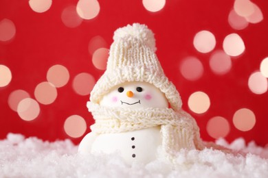 Photo of Cute decorative snowman on artificial snow against red background