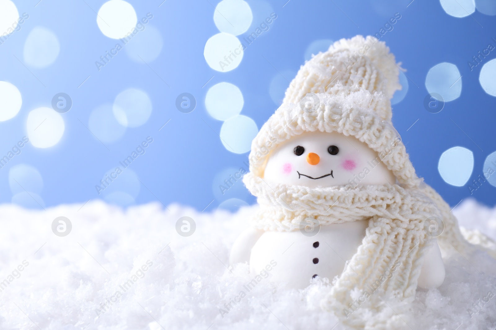 Photo of Cute decorative snowman on artificial snow against light blue background, space for text