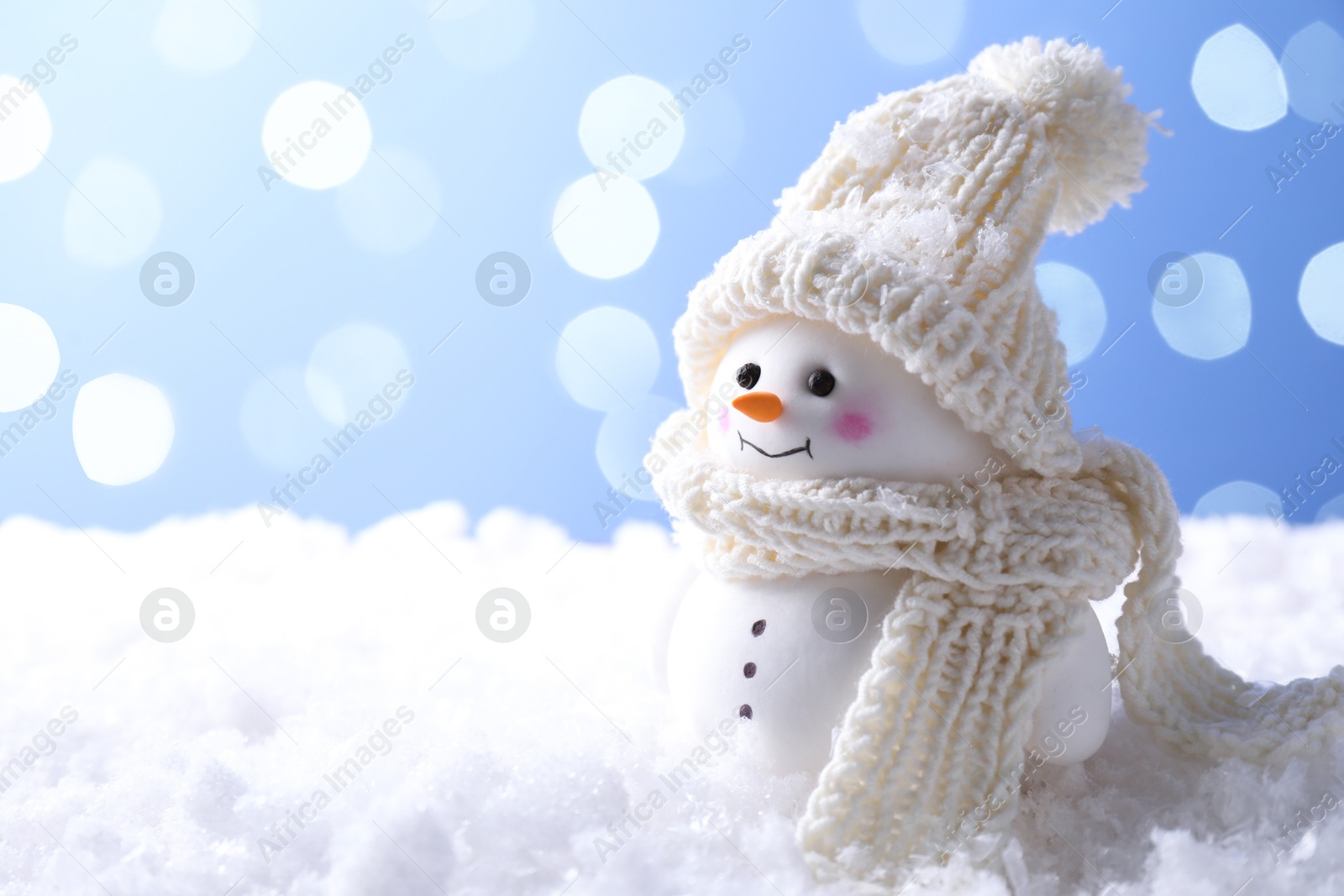 Photo of Cute decorative snowman on artificial snow against light blue background, space for text