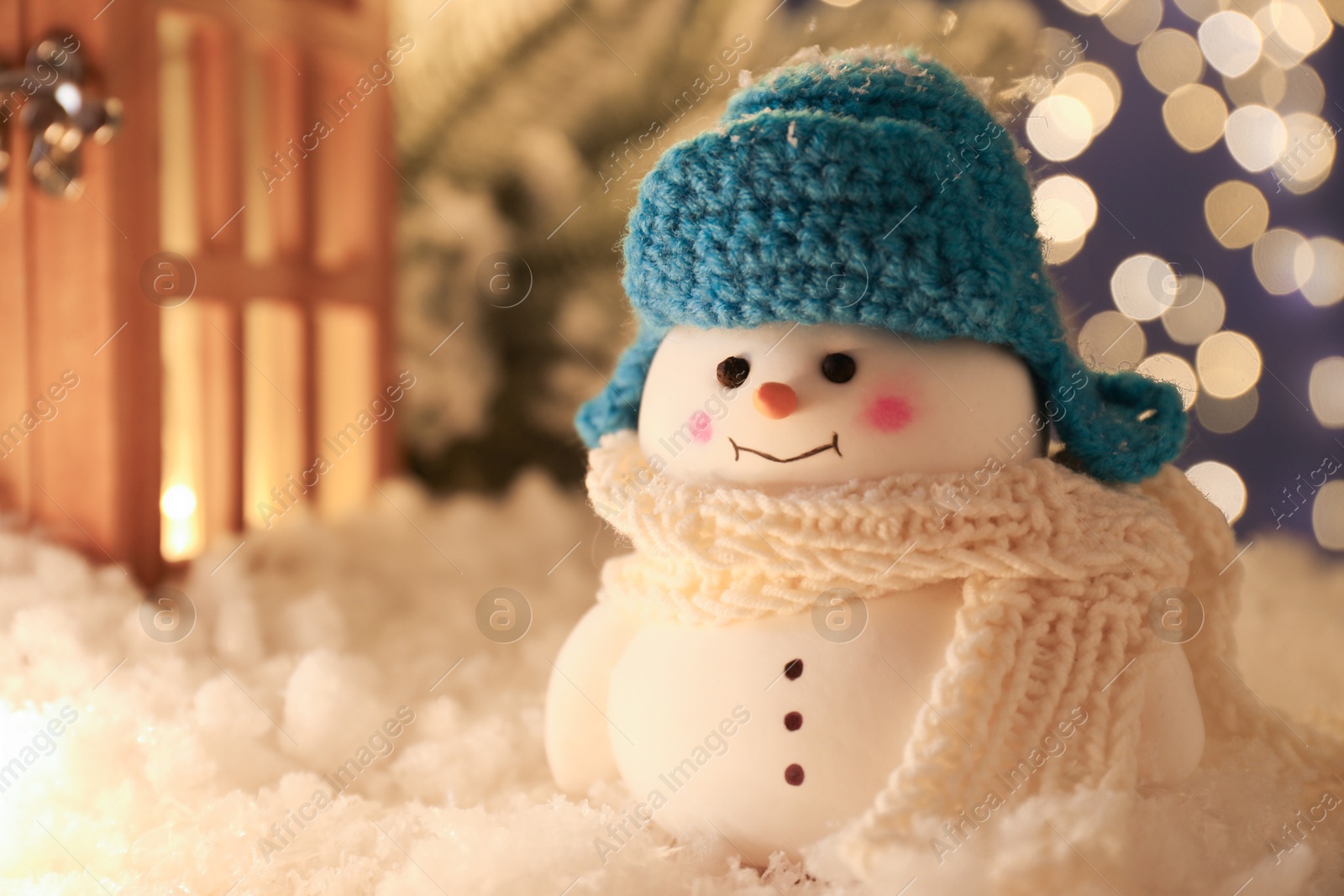 Photo of Cute decorative snowman and other decor on artificial snow against blurred lights, closeup