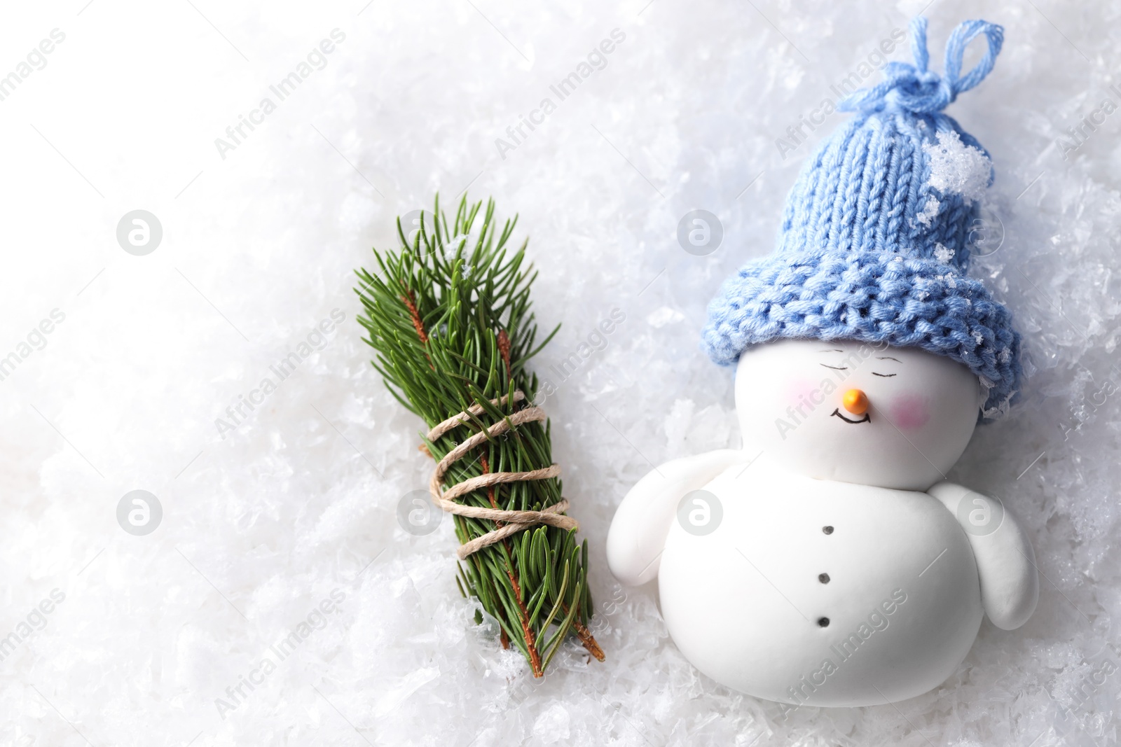 Photo of Cute decorative snowman and fir tree branches on artificial snow, flat lay