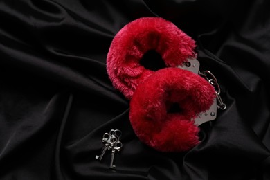 Photo of Red fluffy handcuffs and keys on black fabric