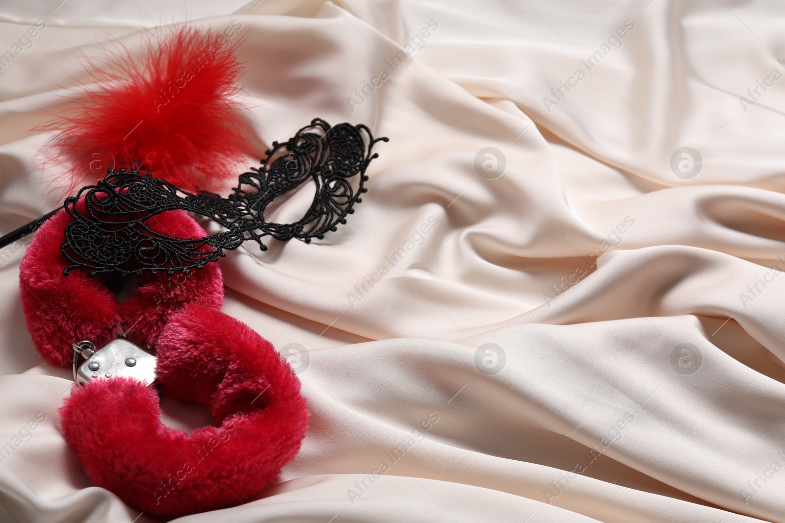 Photo of Red fluffy handcuffs, lace mask and feather on beige fabric. Space for text